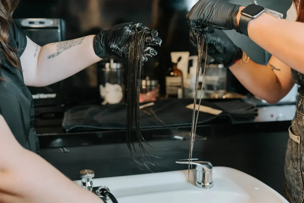 Two people wearing black gloves hold wet strands of dark hair over a white sink, preparing for a hair treatment in an Aveda salon Nashville setting. - True Blue Salon in Nashville, TN