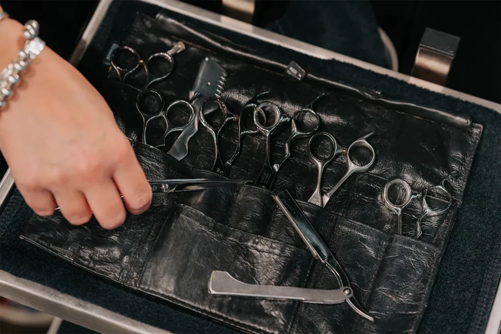 A hand selects a pair of scissors from a black leather case containing various hairdressing scissors and a straight razor, evoking the professional tools used in top Nashville hair salons and Aveda salon Nashville locations offering premium salon gift cards and specials. - True Blue Salon in Nashville, TN