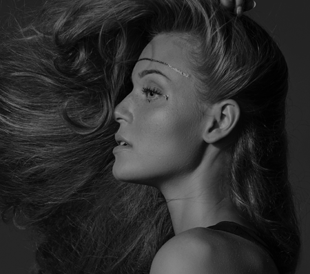 A beautiful black and white side profile photo of a person with long hair being blown to the side. They are wearing a headband across their forehead, showcasing their flawless skin and focused expression. - True Blue Salon | Nashville, TN