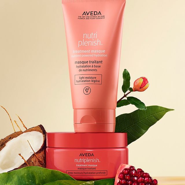 Two Aveda Nutriplenish hair treatment products with natural ingredients, including coconut and pomegranate, displayed on a green leaf. - True Blue Salon | Nashville, TN