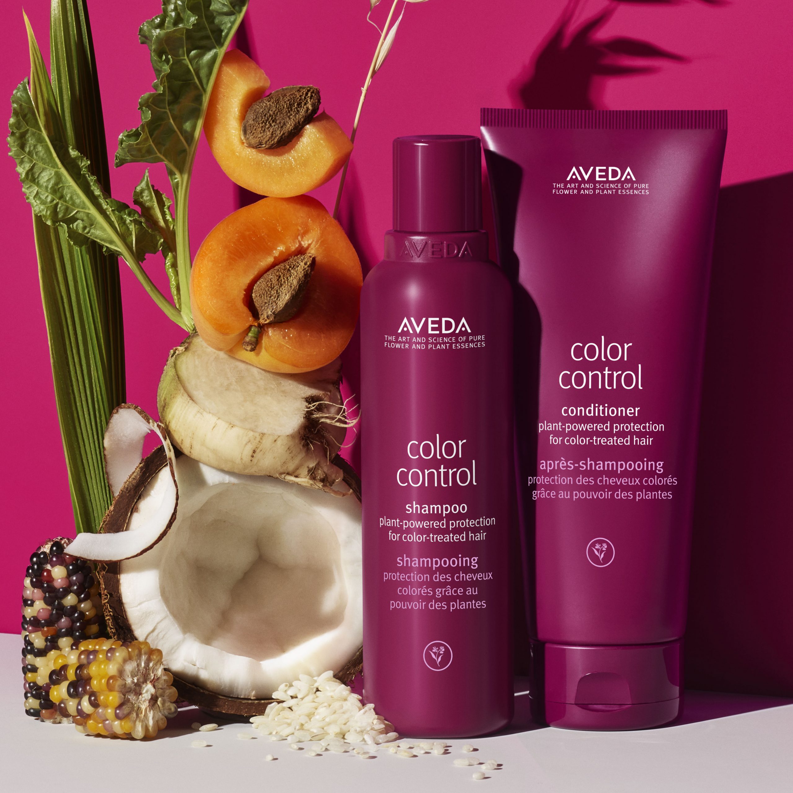 Aveda Color Control shampoo and conditioner bottles are displayed with corn, beet, apricot, and leaves against a pink background. - True Blue Salon | Nashville, TN