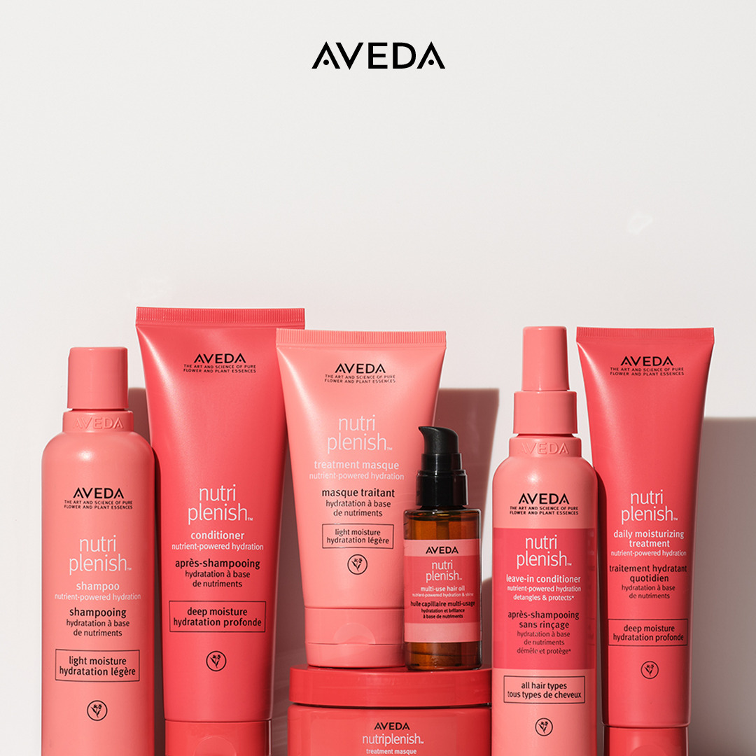 A set of Aveda Nutriplenish hair care products in pink packaging, including shampoo, conditioner, masque, leave-in conditioner, and oil, arranged on a white surface. - True Blue Salon | Nashville, TN